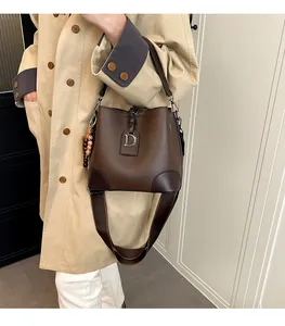 Detalle de bolso saco de cuero marrón oscuro con colgante de letra D y correa tejida