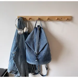Détail d'un sac à dos en jean délavé avec fermeture éclair centrale sur un cintre en bois