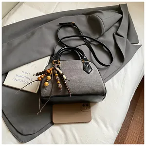 Detail of gray suede shell bag with colorful wooden bead charm and black leather handle