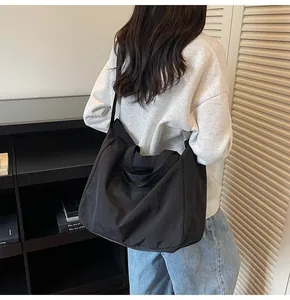 Detail shot of a large black canvas tote bag being worn over the shoulder in a casual setting