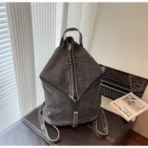 Gros plan d'un sac à dos en denim délavé avec rabat triangulaire et fermeture éclair dorée
