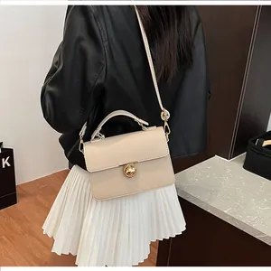 Détail d'un sac à main en cuir beige grainé avec fermoir doré rotatif et bandoulière fine