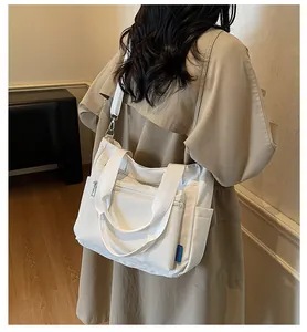 White nylon tote bag with multiple zippers shown on a model for scale and capacity