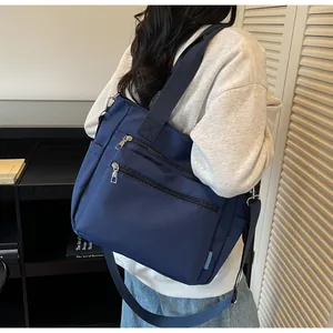 Navy blue nylon tote bag with multiple zippers shown from a side view on a model