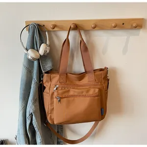 Detail view of brown multi-zipper nylon tote bag hanging on wooden hook in home setting