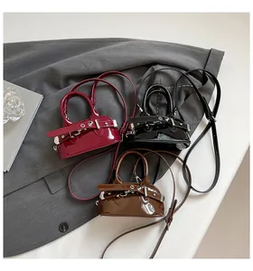 Detail of glossy shell-shaped handbags in burgundy, black and brown with belt buckle accents