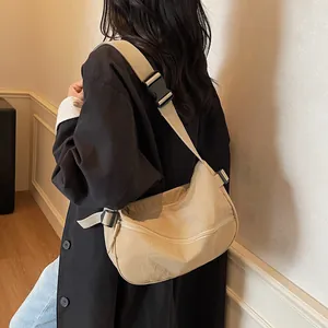 Beige nylon crossbody dumpling bag with wide strap and buckle shown on shoulder