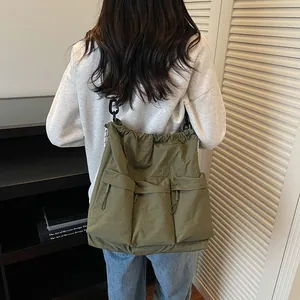 Large khaki nylon tote bag with drawstring and utility pockets shown on a model
