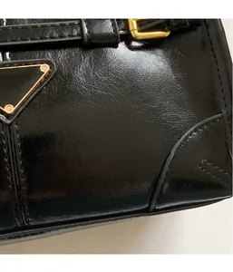 Detail of glossy black leather handbag showing metallic logo and fine stitching texture