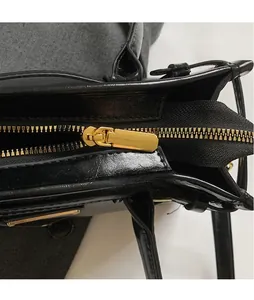 Detail of smooth gold hardware zipper puller on black glossy leather handbag for women