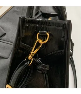 Detailed close-up of glossy black leather handbag with premium gold metal hardware and hooks