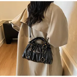 Détail du sac plissé en similicuir noir avec de grands anneaux dorés porté par un mannequin