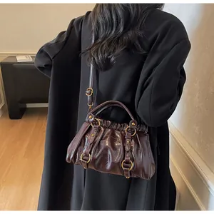 Détail du sac en cuir plissé marron foncé avec boucles dorées porté par un mannequin