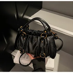 Détail du sac plissé en cuir noir avec anneaux dorés et design à double poignée