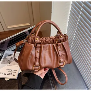 Détail du sac plissé caramel montrant les anneaux en bronze et le logo gaufré