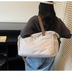 Close-up of a light grey grid travel bag featuring durable brown carry handles and long strap