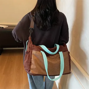 Large dark brown travel tote with yellow check pattern and sky blue straps shown on model