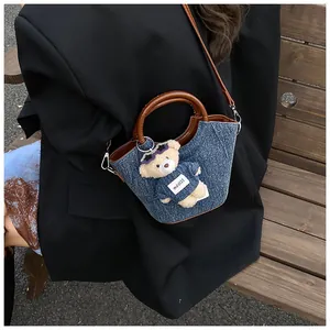 Detail of denim bucket bag with brown leather handles and a plush bear pendant