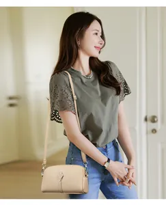 Détail d'un sac bandoulière beige en cuir grainé assorti à un chemisier en dentelle