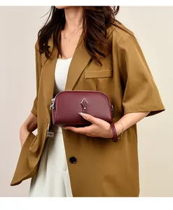 Détail du sac en cuir bordeaux avec fermoir argenté tenu par un mannequin en costume