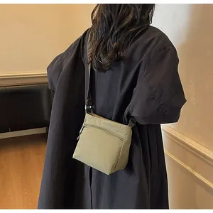 Detail view of olive green nylon crossbody bag with zipper pockets worn by a model