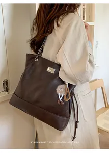 Detail of dark brown tote bag with metal square logo and chain strap on soft PU leather