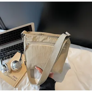 Detail of beige nylon crossbody bag with multiple zippers, laptop, and headphones nearby