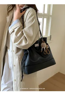 Detail of black leather tote bag with silver chain strap and a brown plush doll charm