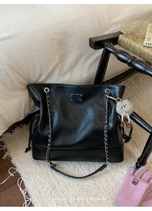 Detail of black leather tote bag featuring silver chain strap and plush pendant accessory