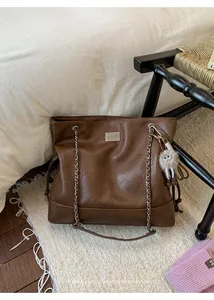 Detail of retro brown leather tote with chain handle and cute monster plush pendant