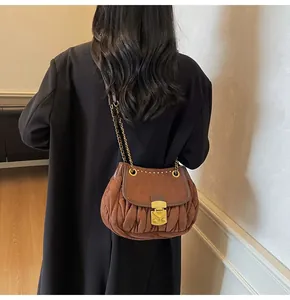 Detail of dark brown pleated crossbody bag with gold metal chain and push-lock closure