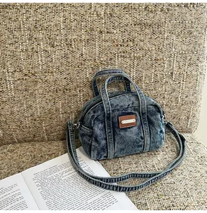 Detail der gewaschenen blauen Denim-Boston-Tasche mit Lederpatch auf beigem Hintergrund