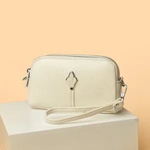 Détail du portefeuille en cuir crème texture litchi avec double zip et décor feuille argent