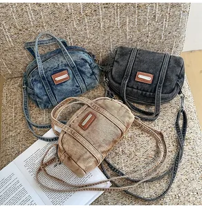 Drei Denim-Boston-Taschen in Blau, Grau und Khaki auf rustikalem Leinenhintergrund