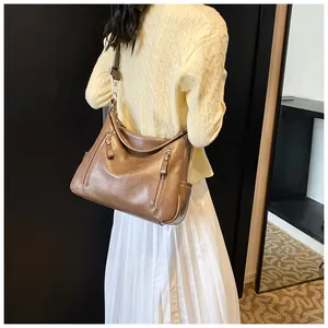 Brown hobo bag with front zip pockets and wide strap shown on a yellow sweater