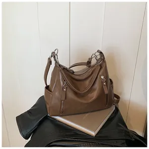 Detail of a brown leather shoulder bag with decorative silver zippers and pockets