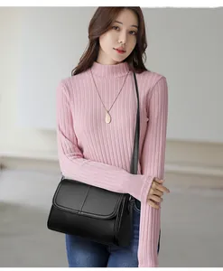 Dettaglio di una borsa a tracolla in pelle nera indossata con un maglione rosa in maglia