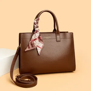 Dettaglio borsa tote in pelle marrone scuro con sciarpa di seta e logo dorato inciso