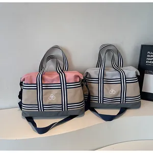 Detail of color-block travel bags in pink and grey with striped webbing handles