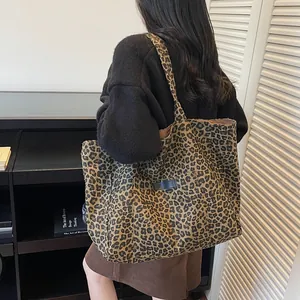 Large leopard print canvas tote bag shown as shoulder bag on model in high fashion setting