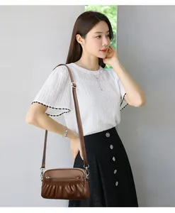 Brown pleated faux leather crossbody bag with adjustable strap worn by model