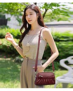 Detail of wine red leather crossbody bag with pleated design worn by a model outdoors