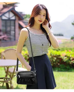 Detail of a black leather pleated crossbody bag with triple zippers in a garden setting