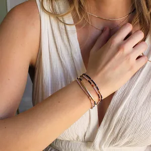 Detail of bohemian layered beaded bracelets with gold curved bar on woman's wrist