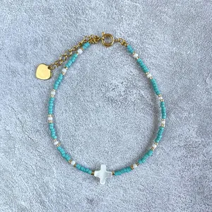Detail of beaded bracelet with turquoise seeds and a white shell cross charm