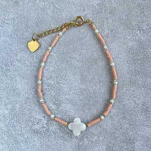 Close-up of pink and white beaded bracelet featuring a mother-of-pearl clover and heart charm