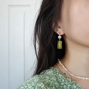 Boucles d'oreilles pendantes en or avec perle blanche et pierre verte sur mannequin
