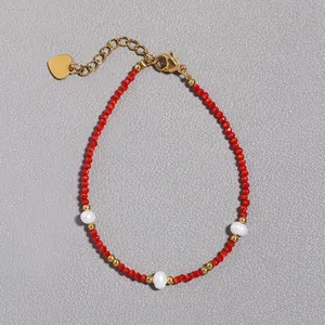 Dettaglio di bracciale con pietre rosse sfaccettate, perle e ciondolo a cuore dorato