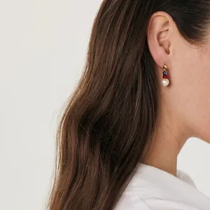Detail of bohemian gold hoop earrings with navy blue, red beads and white pearl on model