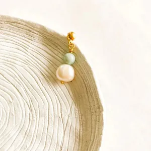 Detail of 18K gold hoop earring with green bead and white baroque pearl on ceramic plate